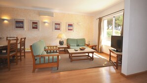 Uma sala de estar com sofá, mesa de centro, TV e área de jantar com cadeiras e mesa.