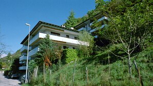 Ein mehrstöckiges Wohngebäude mit Balkonen, umgeben von üppiger Vegetation und blauem Himmel.