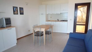 A compact living space with a dining table, chairs, a sofa, a kitchenette, and a television on a cabinet. - Costa Paradiso: Two-room apartment with stunning views (Costa Paradiso)