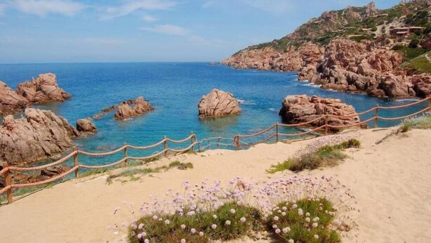 A coastal landscape with rocky formations, a sandy beach, and a wooden fence. - Costa Paradiso: Two-room apartment with stunning views (Costa Paradiso)