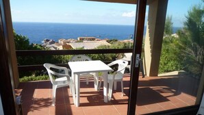 A balcony with a table and chairs, overlooking a coastal view with buildings and the sea. - Costa Paradiso: Two-room apartment with stunning views (Costa Paradiso)
