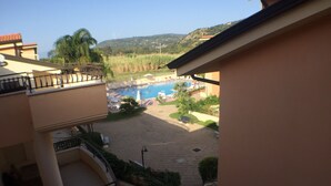 A view of a swimming pool surrounded by lounge chairs and palm trees, with a mountainous landscape in the background. - APARTMENT WITH POOL (Pizzo)