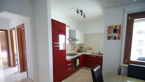 A kitchen with red cabinets, a white countertop, and a dining area with a table and chairs. - APARTMENT WITH POOL (Pizzo)