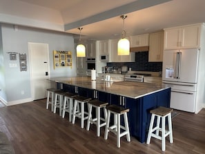 Een moderne keuken met een groot eiland, barkrukken, witte kasten en roestvrijstalen apparatuur.