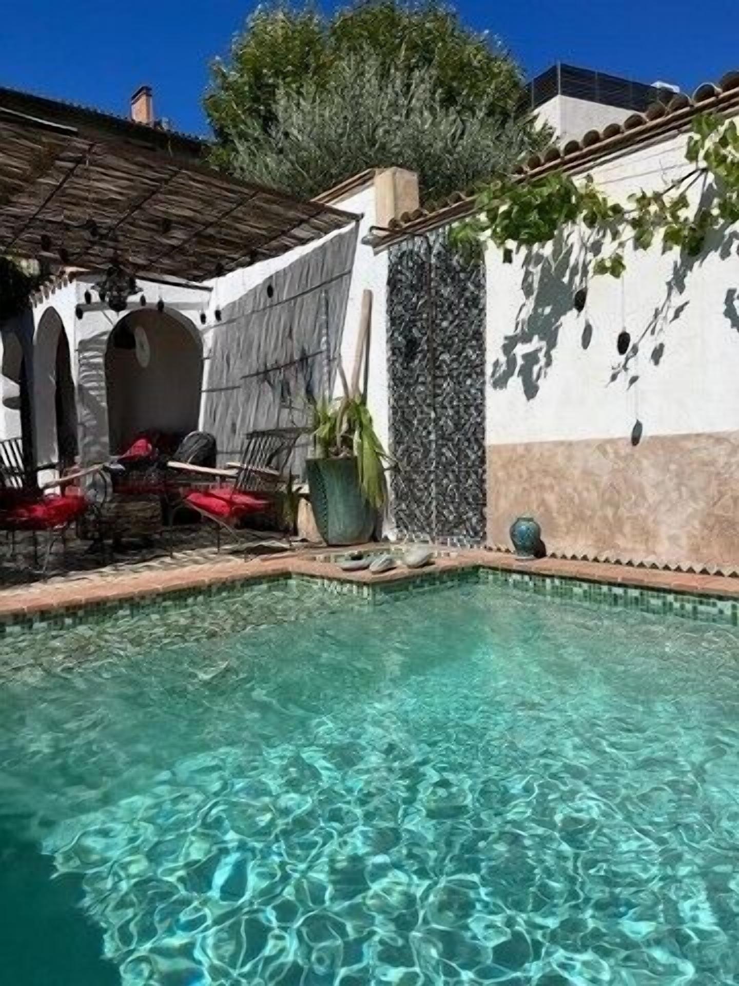 Ein klares Schwimmbecken mit einer gefliesten Kante, umgeben von Sitzgelegenheiten im Freien und einer Pergola.
