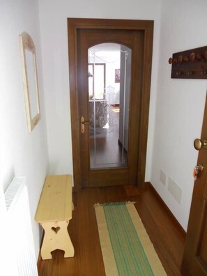 A narrow hallway with a wooden door, a small wooden bench, and a green striped rug on the floor.