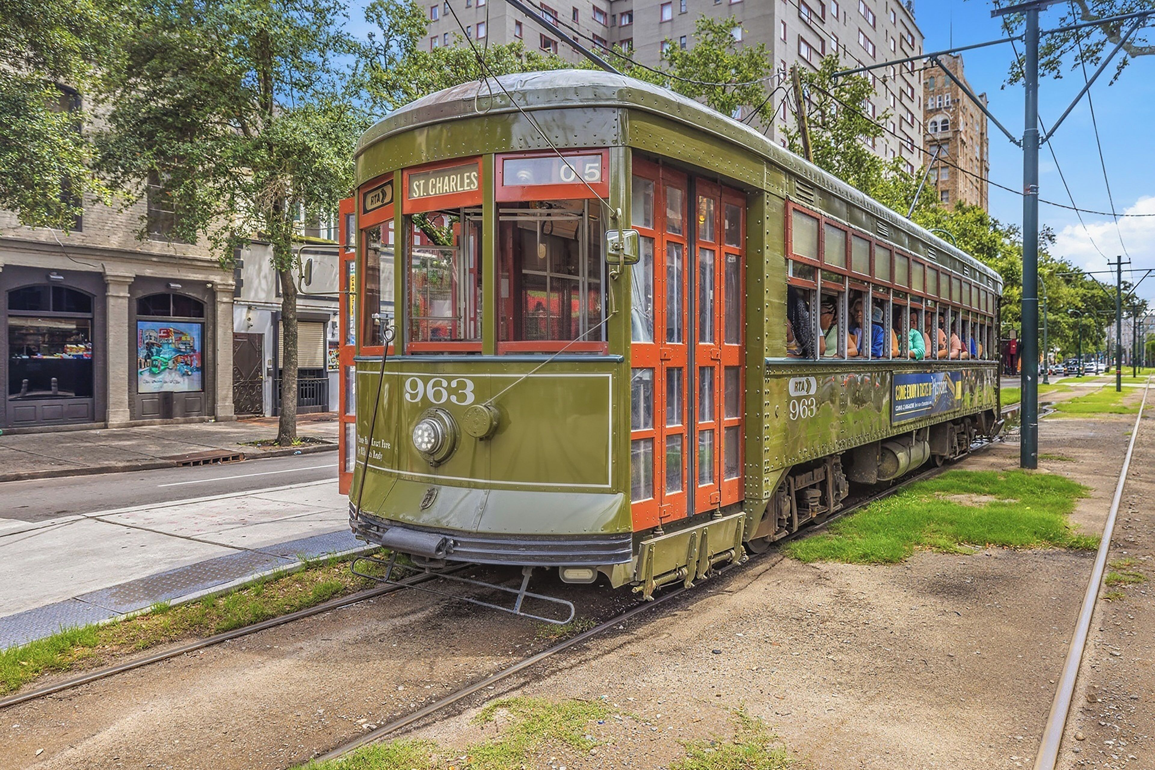 A vintage tram with the number 963 on a track, surrounded by urban buildings and greenery.