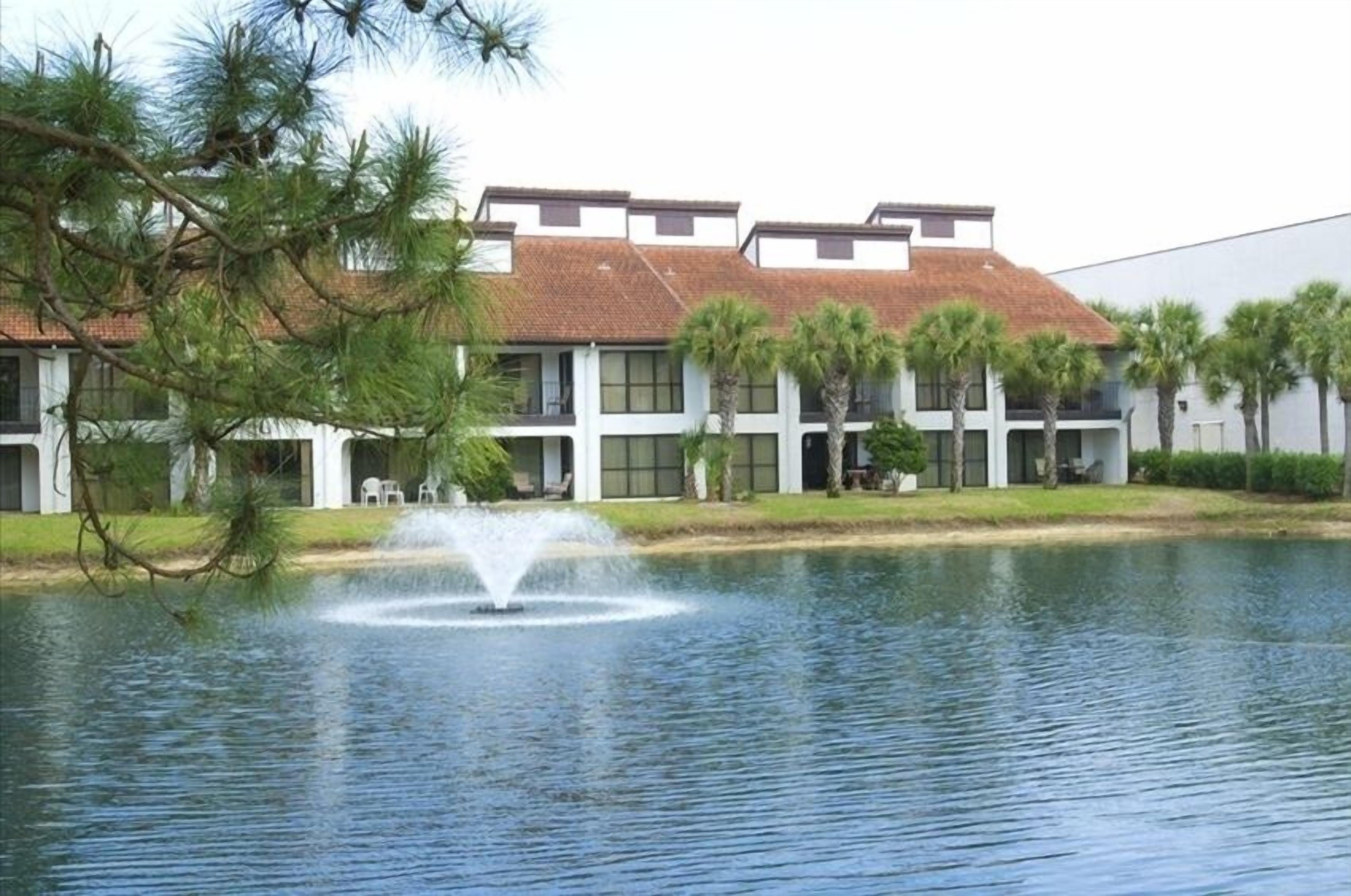 A building with a water fountain in front, surrounded by palm trees and a pond.