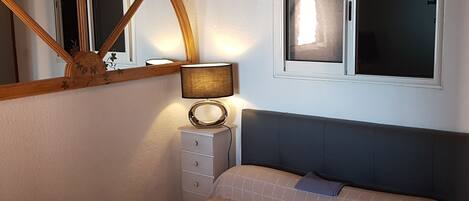 Une chambre à coucher comprenant un lit, une table de chevet avec une lampe, une commode, une fenêtre et un miroir.