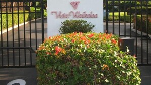 Ein Schild mit dem Text "Vista Waikoloa", umgeben von einem schwarzen Metallzaun und einem Blumenbeet.