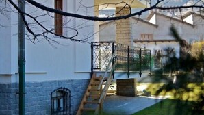 Un mur de pierre, une échelle en bois et un portail en métal dans une cour.