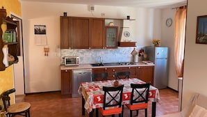 Une cuisine compacte avec des meubles en bois, un lave-vaisselle encastré, une cuisinière à gaz et un réfrigérateur. On y trouve une table à manger avec quatre chaises et un petit canapé dans le salon attenant.