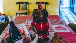 Une table à manger recouverte d’une nappe à carreaux rouges et blancs, une bouteille de vin, un panier et un pot en bois.