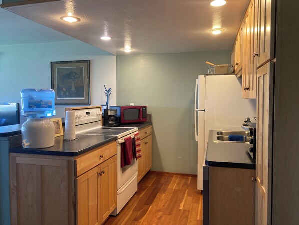 A compact kitchen with wooden cabinets, a white refrigerator, a microwave, a stove, and a water dispenser.