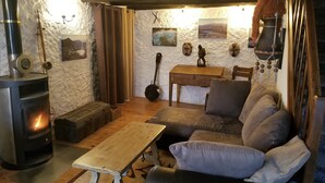 A cozy living room with a wood-burning stove, a sofa, a wooden table, and a guitar against the wall.