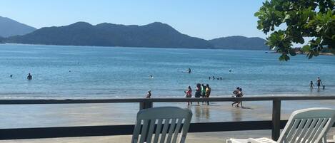 A wooden deck with white chairs overlooking a beach with people swimming and walking.