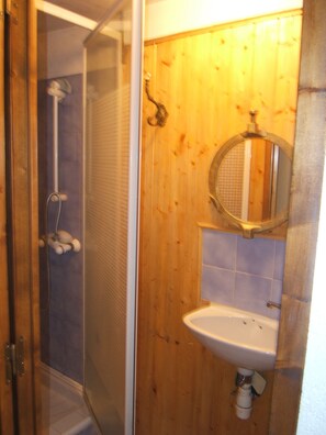 Ett badrum med en väggpanel i trä, en duschkabin med glasväggar, ett handfat och en spegel.