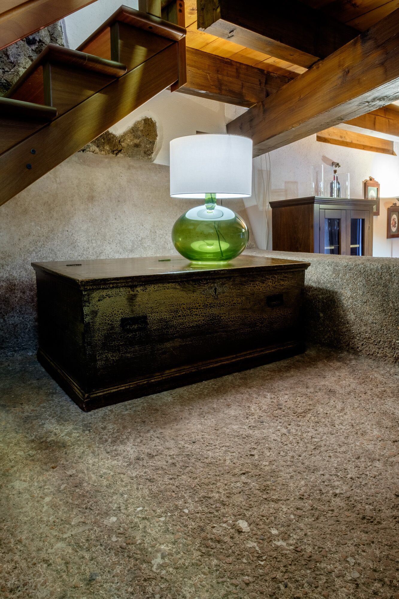 Una stanza rustica con un baule di legno, una lampada verde e una parete in pietra.