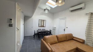 Uma sala de estar moderna com sof á de couro, área de jantar com mesa e cadeiras, e um claraboia acima.