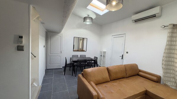 A modern living room with a leather sofa, a dining area with a table and chairs, and a skylight above.