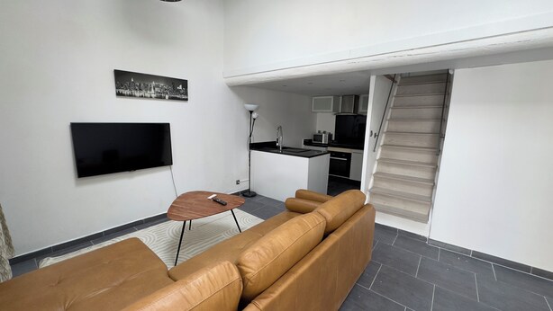 Uma sala de estar moderna com um sofá de couro marrom, uma TV de tela plana na parede e uma pequena mesa de madeira com um controle remoto.