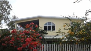 Une maison à la façade jaune, avec une clôture blanche en bois et des plantes en fleurs.