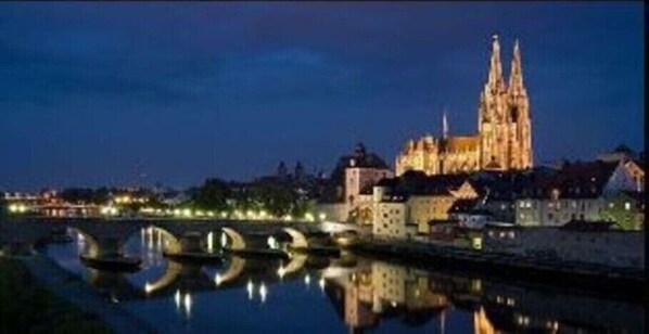 Una catedral con una aguja alta, una masa de agua con barcos y un paisaje urbano al fondo.