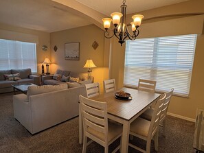 A dining area with a wooden table and chairs, a chandelier, and a sofa set in the background. - 6 bed comfort, close to the parks & superb lake view with private pool (Kissimmee)