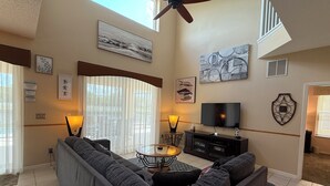 Een woonkamer met een hoekbank, een televisie, kunstwerken en een plafondventilator.