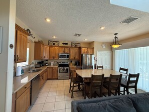 A kitchen with wooden cabinets, a stainless steel refrigerator, a microwave, and a dining area with a table and chairs. - 6 bed comfort, close to the parks & superb lake view with private pool (Kissimmee)