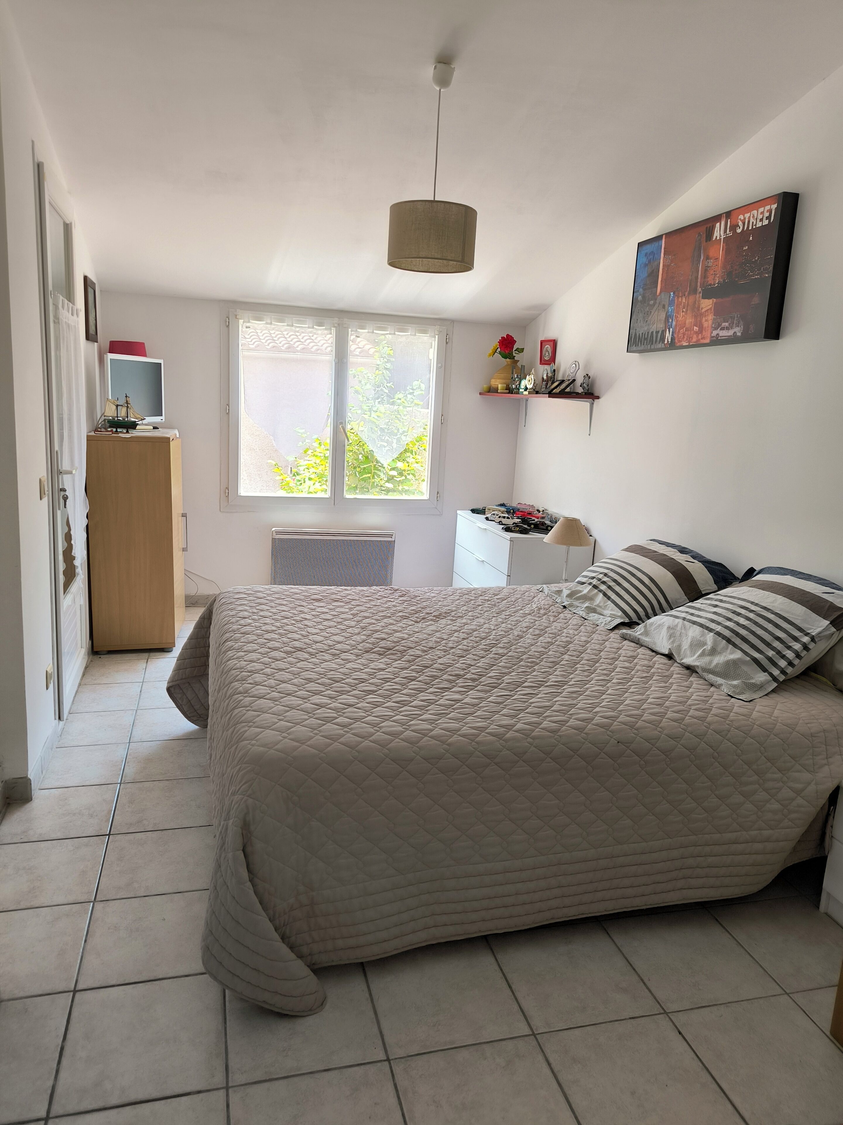 A bedroom with a bed, a desk, a chair, a window, and a wall-mounted picture.