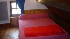 A bedroom with a wooden ceiling, a bed with a red blanket, a window with blue curtains, and a small picture on the wall. - Quiet chalet 5/7 places WIFI (Campan)
