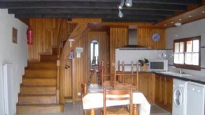 A kitchen with wooden cabinets, a dining table with chairs, a washing machine, and a staircase leading to another level. - Quiet chalet 5/7 places WIFI (Campan)