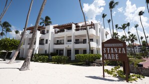 A beachfront hotel with multiple balconies, palm trees, and a sandy beach. - Fantastic Condo on the Beach. Relax and enjoy the breeze !!! (Bavaro)