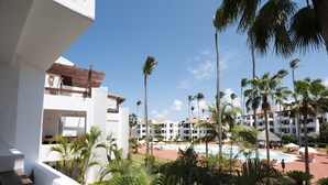 A resort with a pool area surrounded by palm trees and a view of hotel buildings. - Fantastic Condo on the Beach. Relax and enjoy the breeze !!! (Bavaro)