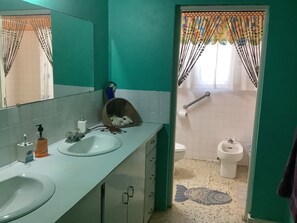 Un baño con dos lavabos, un inodoro y un bidé. Se ve un espejo sobre los lavabos y un perchero de toallas.