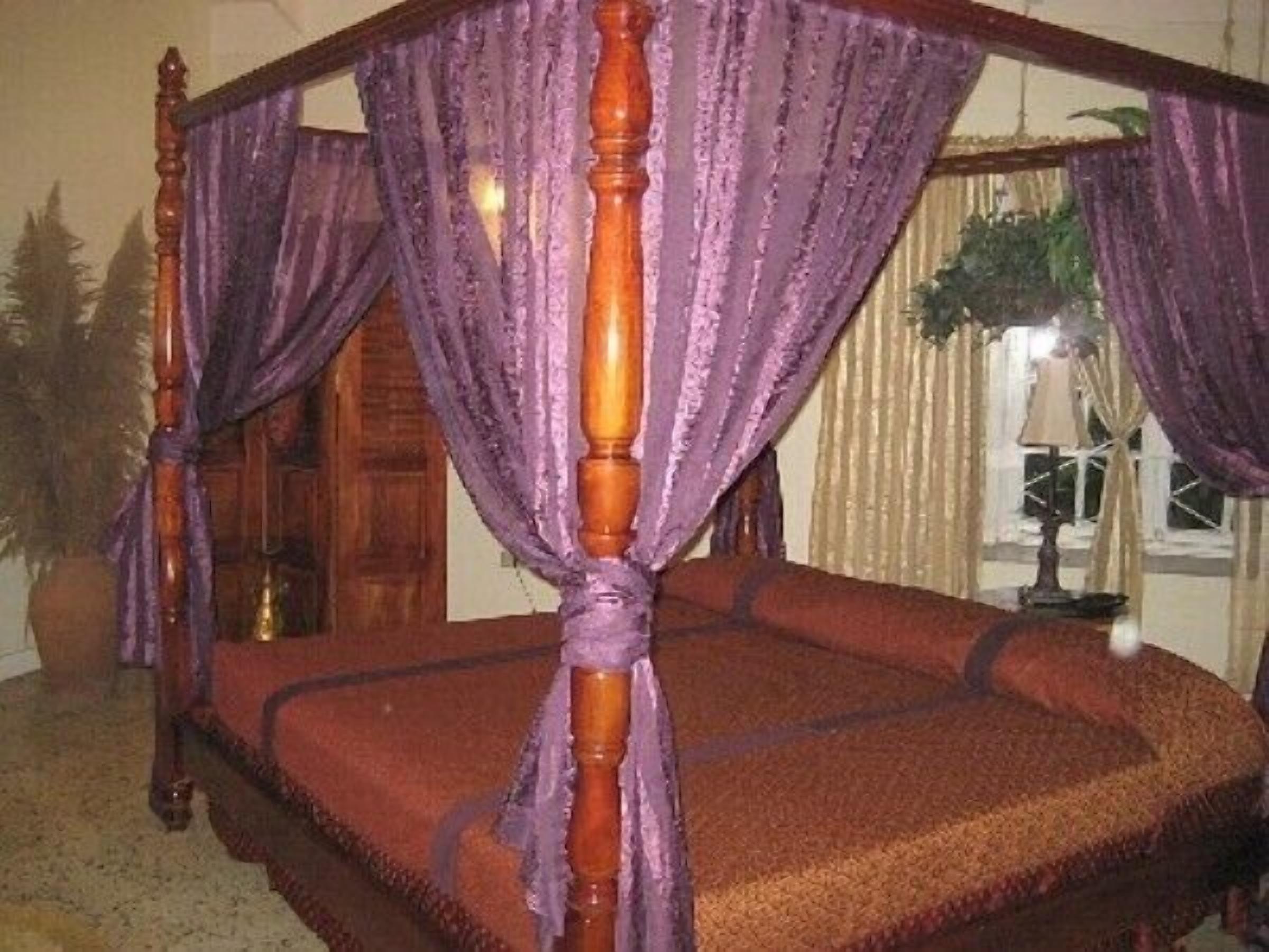 A four-poster bed with purple drapes, a red bedspread, and a wooden headboard.