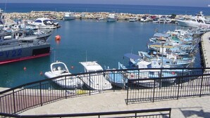 Un puerto deportivo con varias embarcaciones amarradas, un barco grande a la izquierda y un cielo azul despejado.