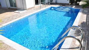 Una piscina rectangular de agua cristalina, rodeada de baldosas de piedra y barandales de metal.
