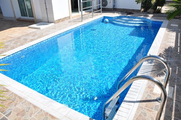 Una piscina rectangular de agua cristalina, rodeada de baldosas de piedra y barandales de metal.