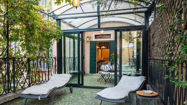 A glass-enclosed patio with two lounge chairs and a small table, surrounded by a metal fence and greenery. - Charming 4 bedrooms Apartment with Amazing Terrace and Fairytale Garden (Venezia)