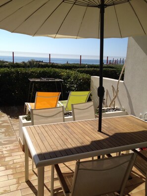 Patio esterno con tavolo e sedie di legno, un ombrellone e vista sul mare.