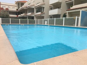Una piscina con recinzione bianca, circondata da edifici a più piani con balconi.