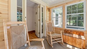 Een houten interieur met twee schommelstoelen en een bank bij grote ramen.