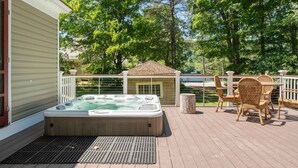 Een hottub op een houten terras met rieten meubels en uitzicht op bomen en een gebouw.