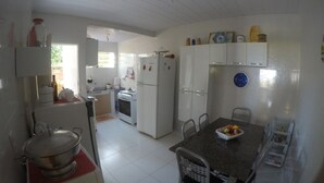 A compact kitchen with white cabinets, a dining table with chairs, a refrigerator, and a stove. - Seafront house, paradise with privacy - ITACIMIRIM - 06 bedrooms and 4 suites (Camaçari)