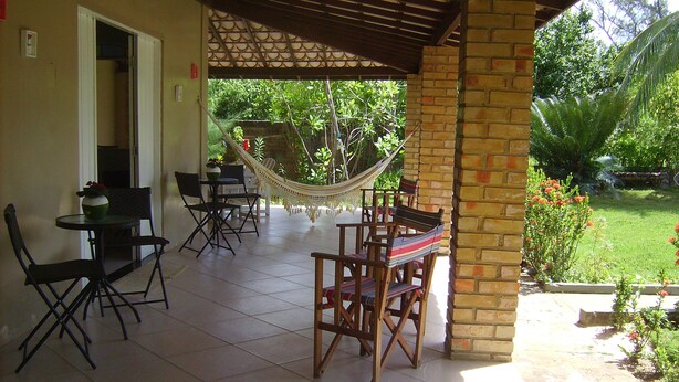 A covered patio area with a table and chairs, a hammock, and a view of a garden. - Seafront house, paradise with privacy - ITACIMIRIM - 06 bedrooms and 4 suites (Camaçari)