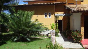 A house with a tiled roof, a satellite dish, and a garden with palm trees and flowers. - Seafront house, paradise with privacy - ITACIMIRIM - 06 bedrooms and 4 suites (Camaçari)