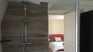 Een moderne badkamer met een douche, houten wand en een blik op een slaapkamer met een bed en een rode hoofdbord.