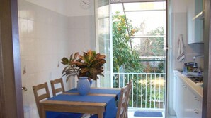 A small dining area with a table and chairs, a potted plant, and a view of a balcony with a railing and some greenery. - Cozy Apt for 4/6 persons near the sea well linked with the center of Rome (Lido di Ostia)